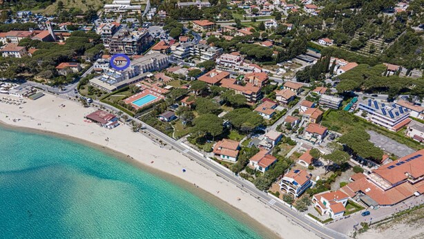 Vista aérea de un pueblo costero con playa, edificios residenciales y una piscina.