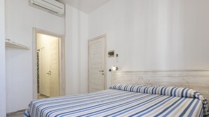 Un dormitorio con una cama, cabecera de madera, una puerta y una lámpara fijada a la pared.