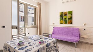 Un comedor con una mesa dispuesta para dos personas, un sofá morado y un ventanal con cortinas.