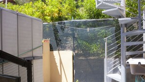 A corner of a building with a beige wall, a metal staircase, and a mesh fence.