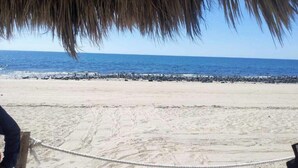 A beach with a rope barrier, a thatched roof structure, and a rocky shoreline. - Condo Mirador with Rooftop Ramada Near Sea of Cortéz, El Malecon, and Manny's. (Puerto Peñasco)