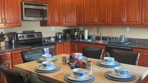 A kitchen with wooden cabinets, a microwave, a stove, and a dining table set with blue and white plates and cups. - Condo Mirador with Rooftop Ramada Near Sea of Cortéz, El Malecon, and Manny's. (Puerto Peñasco)