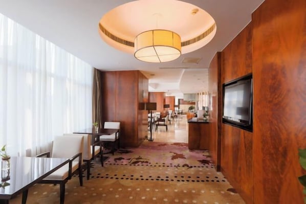 A hotel lobby with a dining area, a TV mounted on the wall, and a large circular ceiling light.