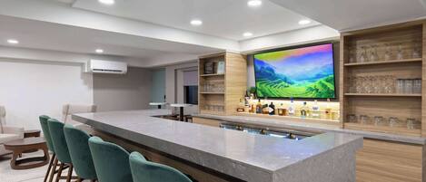 Una cocina moderna con barra, taburetes y un televisor de pantalla plana grande.