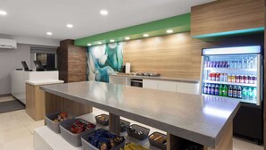 Eine moderne Küchenzeile mit einer langen Arbeitsplatte, einem mit Getränken gefüllten Kühlschrank und Körben mit Snacks.