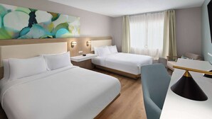 Ein Hotelzimmer mit zwei Betten, einem Schreibtisch, einem Stuhl und einem großen, abstrakten Gemälde an der Wand.