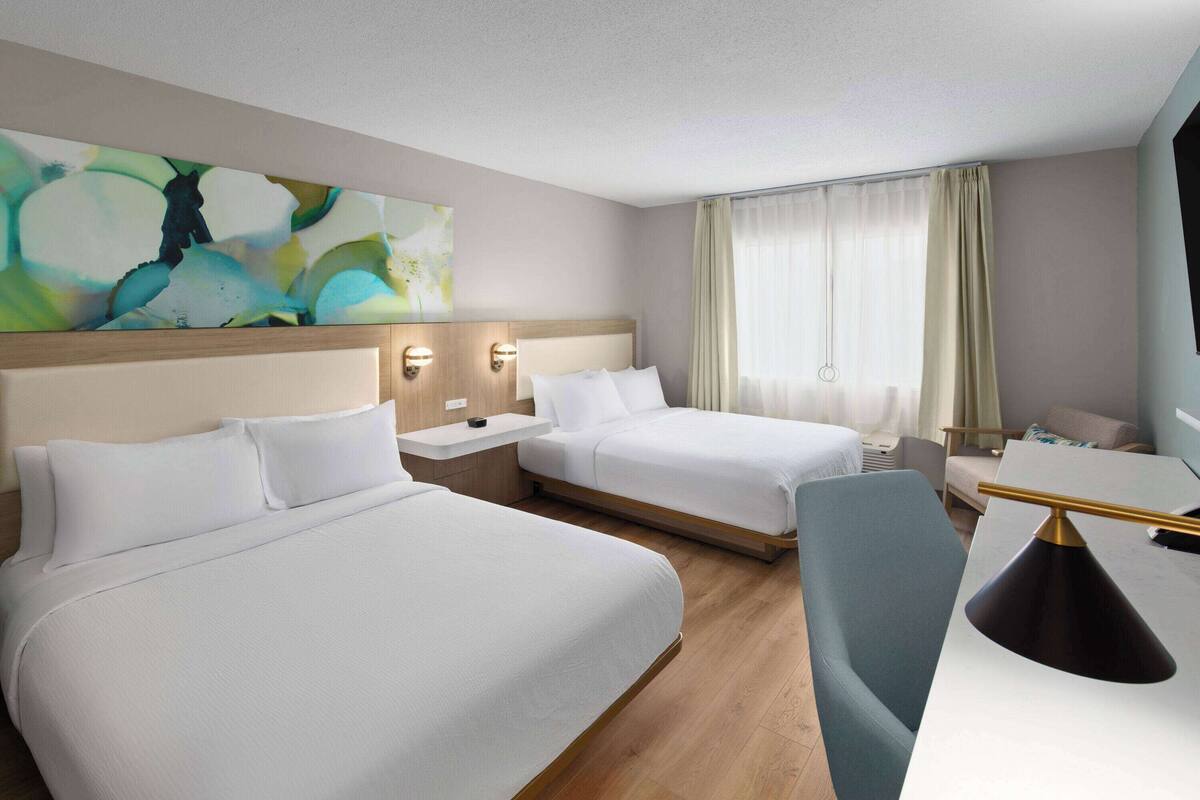 A hotel room with two beds, a desk, a chair, and a large abstract painting on the wall.