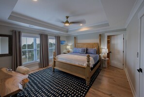 A spacious bedroom with a large bed, a ceiling fan, and a view of the outdoors through the window. - Tybee Ocean View & Private Pool - 1B Oceanview Court (Tybee Island)