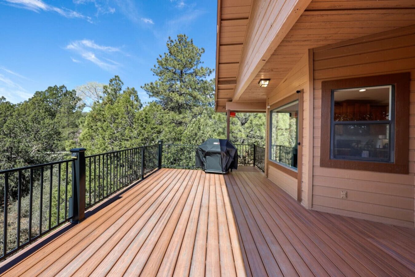 A wooden deck with a grill, surrounded by a metal railing, overlooking a forested area.