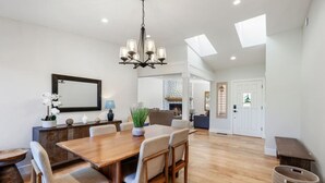 A spacious dining area with a wooden table, chairs, and a chandelier. There is a fireplace in the background, and the room has a high ceiling with skylights. - Summit Lodge- Sleeps 10, 4 Full Bath, Pet Friendly (Prescott)