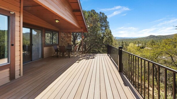 A wooden deck with a railing, a table and chairs, and a view of a forested landscape. - Summit Lodge- Sleeps 10, 4 Full Bath, Pet Friendly (Prescott)