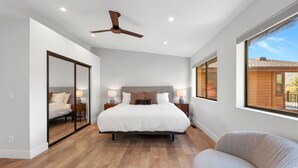 A bedroom with a large bed, a ceiling fan, and a view of a wooden building through a window. - Summit Lodge- Sleeps 10, 4 Full Bath, Pet Friendly (Prescott)