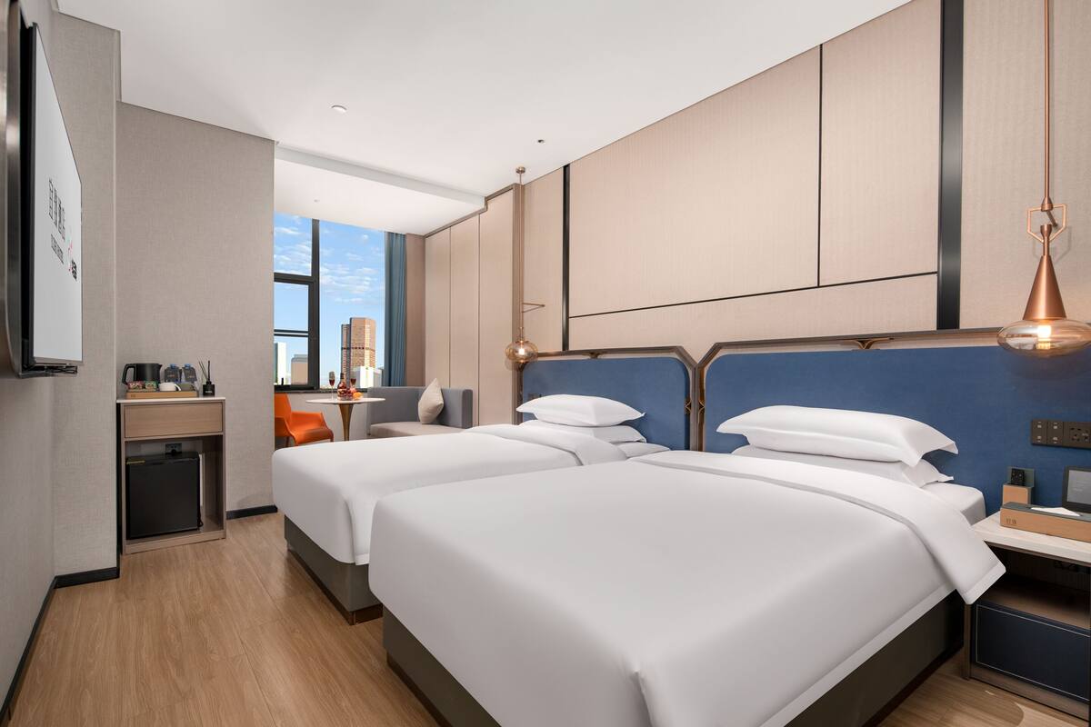 Une chambre d’hôtel avec deux lits, un bureau, une chaise et une vue sur la ville.