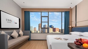 A hotel room with a bed, a sofa, a dining table with fruit, and a city view. - Yi Zhi Hotel (Pearl River Xincheng Store, Wuyangcun Metro Station, Guangzhou) (Guangzhou)