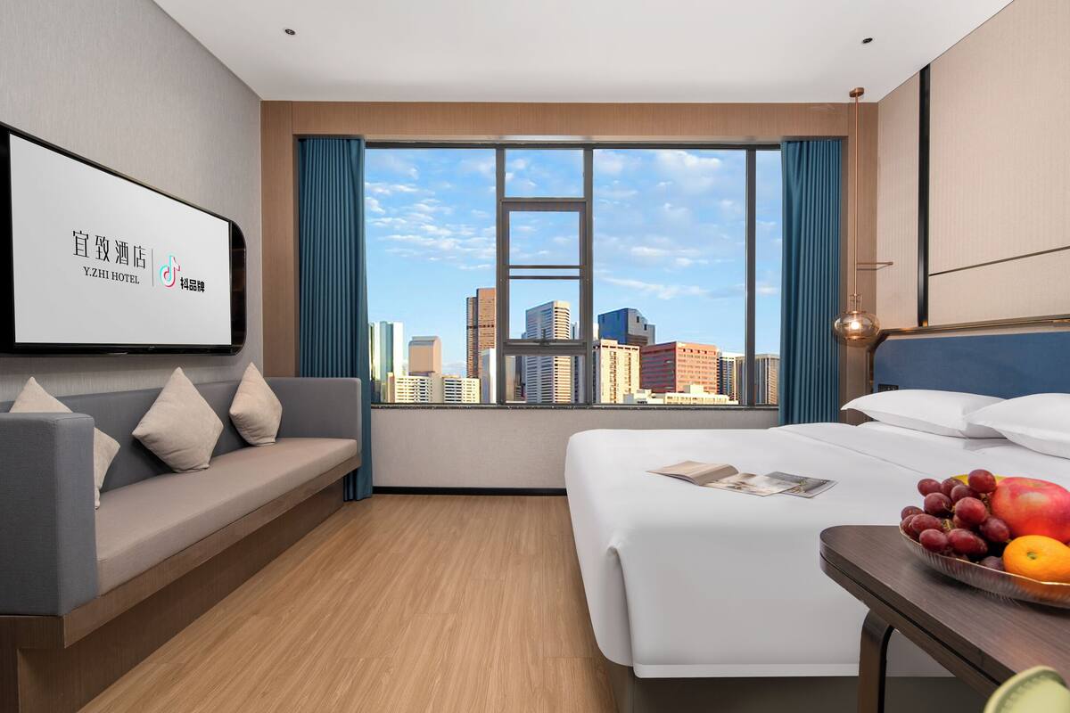Une chambre d’hôtel avec un lit, un canapé, une table à manger avec des fruits et une vue sur la ville.