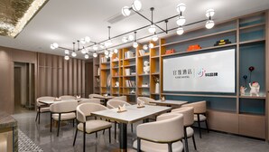 A modern hotel conference room with tables and chairs, a projection screen, and bookshelves. - Yi Zhi Hotel (Pearl River Xincheng Store, Wuyangcun Metro Station, Guangzhou) (Guangzhou)