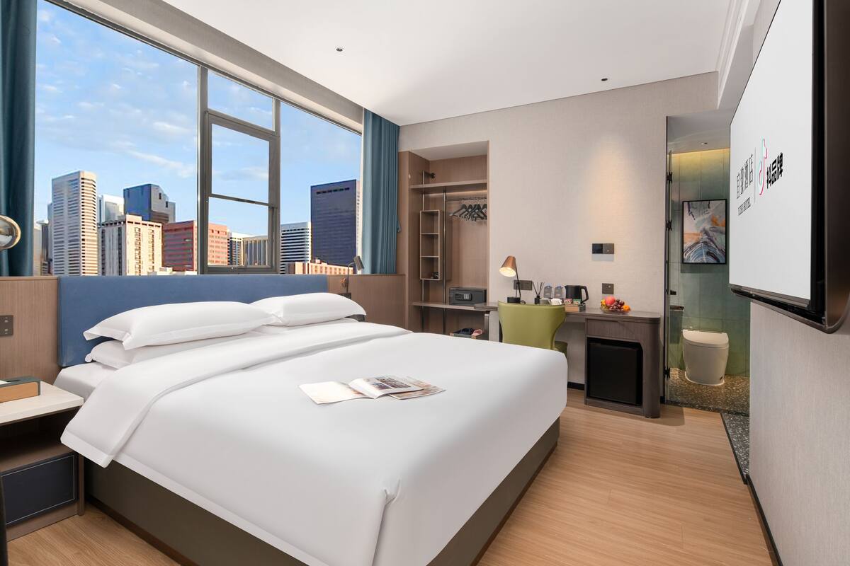 Une chambre d’hôtel moderne dotée d’un grand lit, d’un bureau et offrant une vue sur le panorama urbain.