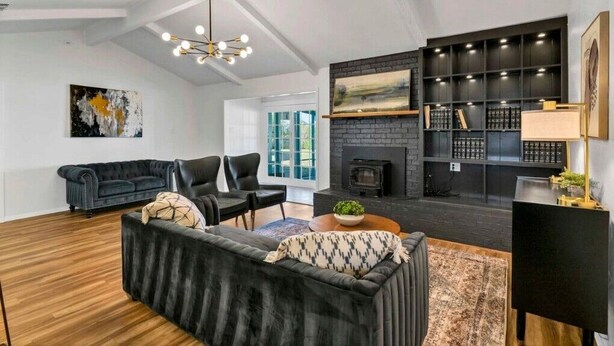 A modern living room with a fireplace, black shelving, and a large window.