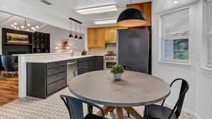 A modern kitchen with a central island, pendant lighting, and a dining area with a round table and chairs.