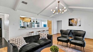 A modern living room with a black sofa, two leather chairs, a coffee table with a plant, and a contemporary chandelier.