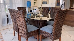 A dining area with a round glass table surrounded by wicker chairs with grey cushions. - Crea recuerdos inolvidables en este alojamiento único y familiar. (Sosúa)