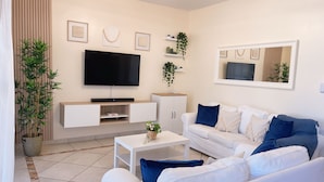 A modern living room with a flat-screen TV, white sofas, a coffee table, and decorative plants. - Crea recuerdos inolvidables en este alojamiento único y familiar. (Sosúa)