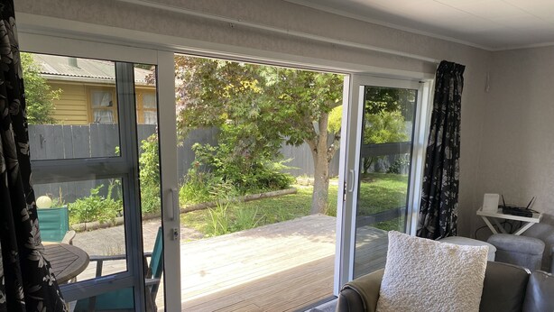 A living room with a sliding glass door leading to a deck, a sofa with a cushion, and a small table with a laptop.