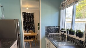 A compact kitchen with a refrigerator, sink, and oven. There is a dining area with a table and chairs visible through an open doorway.