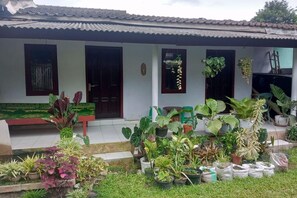 A house with a tiled roof, a front porch with a bench, and various potted plants both on the porch and in the yard. - Homestay Wijaya Mulya By Zuzu (Borobudur)