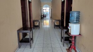 A hallway with tiled floors, two wooden benches, and a water dispenser on the right. - Homestay Wijaya Mulya By Zuzu (Borobudur)
