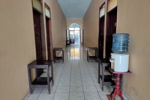 A hallway with tiled floors, two wooden benches, and a water dispenser on the right. - Homestay Wijaya Mulya By Zuzu (Borobudur)