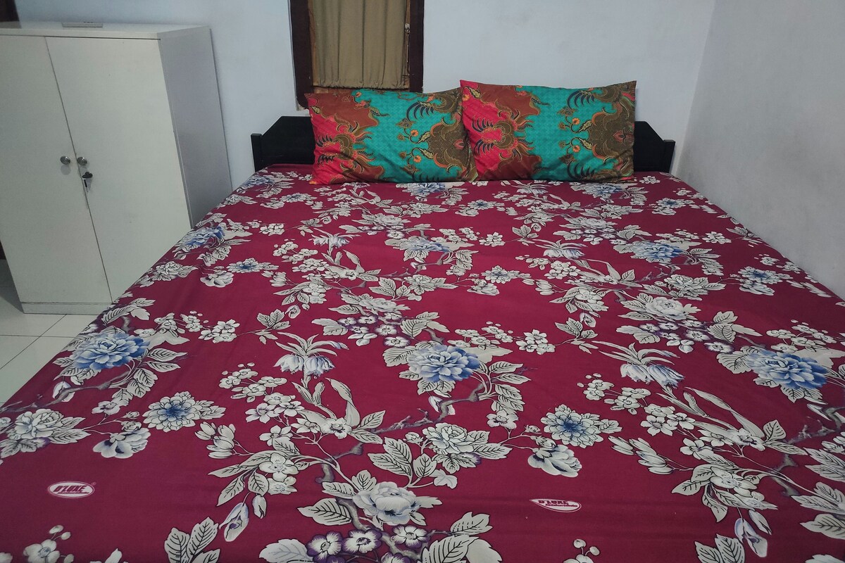A bed with a floral-patterned bedspread, a wardrobe, and a window with a curtain.