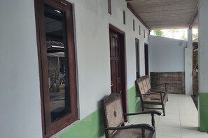 A covered outdoor area with a tiled floor, wooden benches, and a wall with a green baseboard. - Homestay Wijaya Mulya By Zuzu (Borobudur)