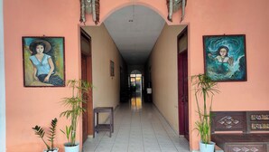 A hallway with two paintings, potted plants, and a bench. - Homestay Wijaya Mulya By Zuzu (Borobudur)