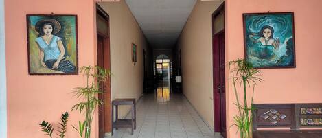 A hallway with two paintings, potted plants, and a bench.