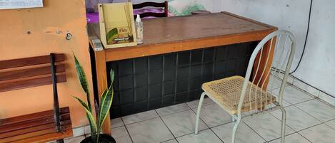 A reception area with a wooden counter, a white metal chair, a potted plant, and a bulletin board with numbers.
