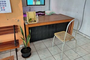 A reception area with a wooden counter, a white metal chair, a potted plant, and a bulletin board with numbers. - Homestay Wijaya Mulya By Zuzu (Borobudur)
