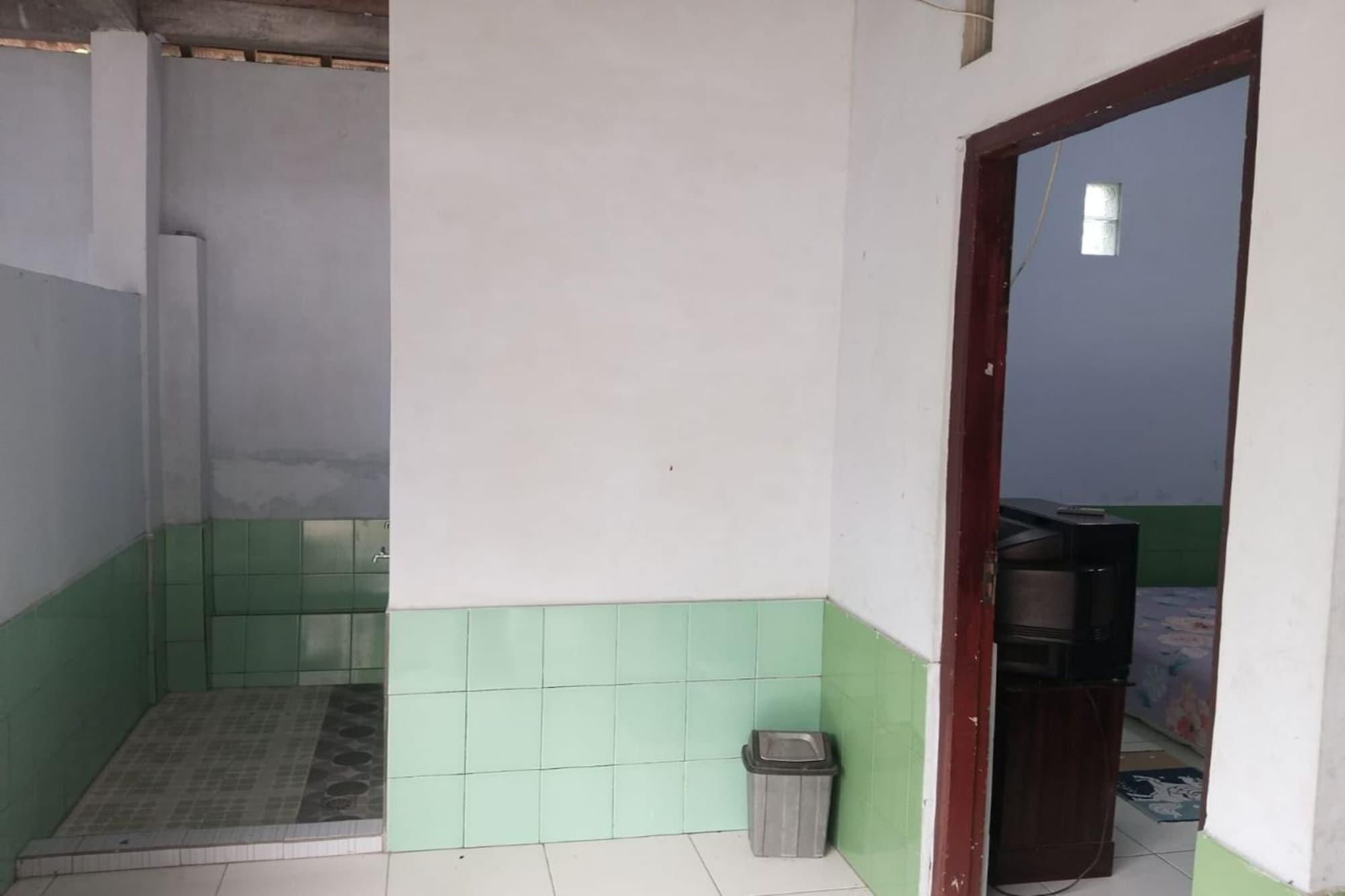 A small, sparsely furnished room with a tiled floor, a trash bin, and a television in the corner.