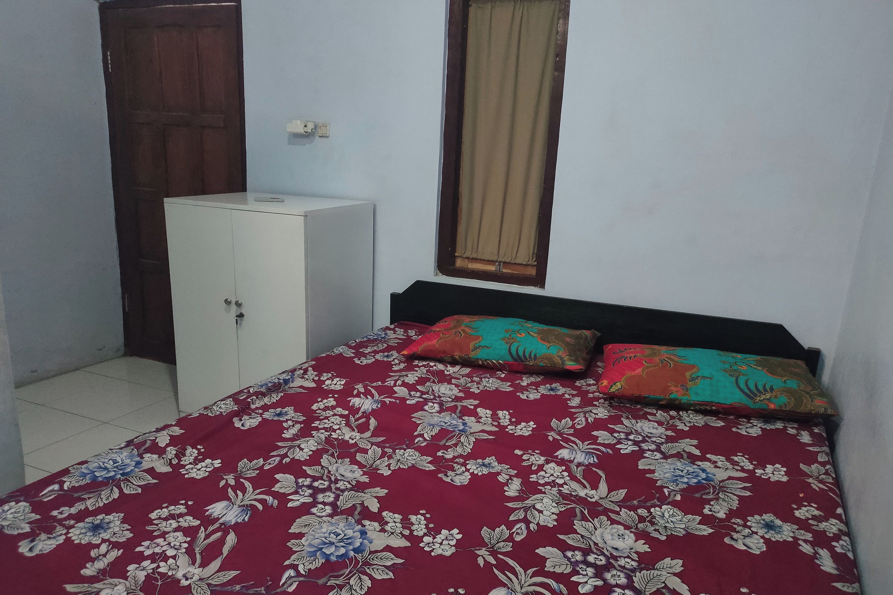 Un dormitorio con cama, armario, ventana con cortinas y suelo de baldosas.