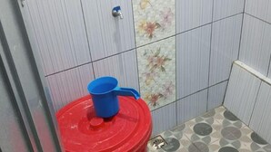 Un baño pequeño con un inodoro, un bote de basura rojo y una taza azul.