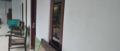 A corridor with wooden chairs lined up against a wall, a green sofa, and a door leading to an outdoor area.