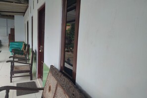 A corridor with wooden chairs lined up against a wall, a green sofa, and a door leading to an outdoor area. - Homestay Wijaya Mulya By Zuzu (Borobudur)