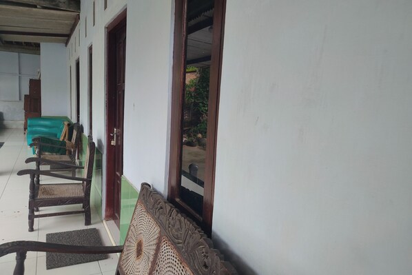 A corridor with wooden chairs lined up against a wall, a green sofa, and a door leading to an outdoor area.