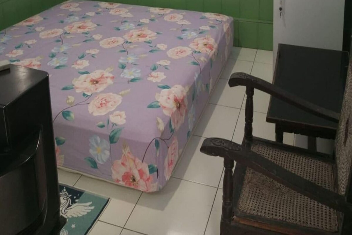 A small room with a bed, a chair, a television, and a cabinet.