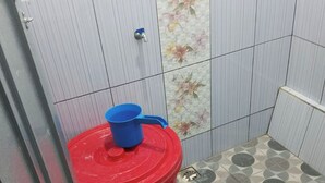 Un baño pequeño con inodoro, un basurero rojo y un grifo instalado en la pared.