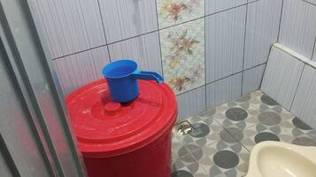 Um banheiro pequeno com vaso sanitário, uma lixeira vermelha e uma torneira fixada na parede.
