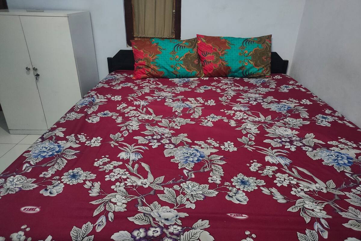 A bed with a floral-patterned bedspread, a wardrobe, and a window with a curtain.