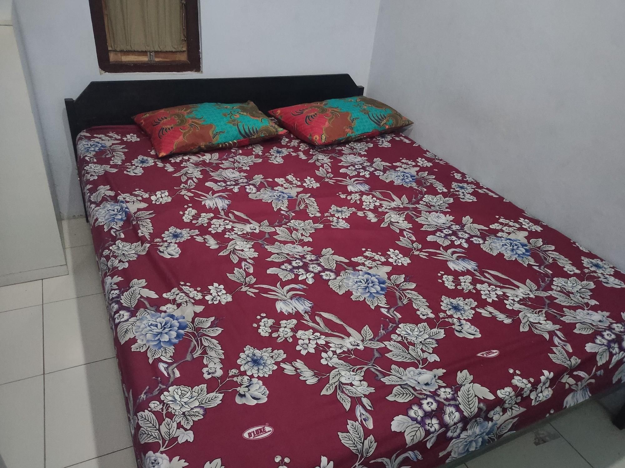 Een bed met een bloemenprint sprei en twee decoratieve kussens.