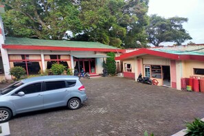 A building with a green roof, a paved courtyard, and a parked car. - Homestay Wijaya Mulya By Zuzu (Borobudur)