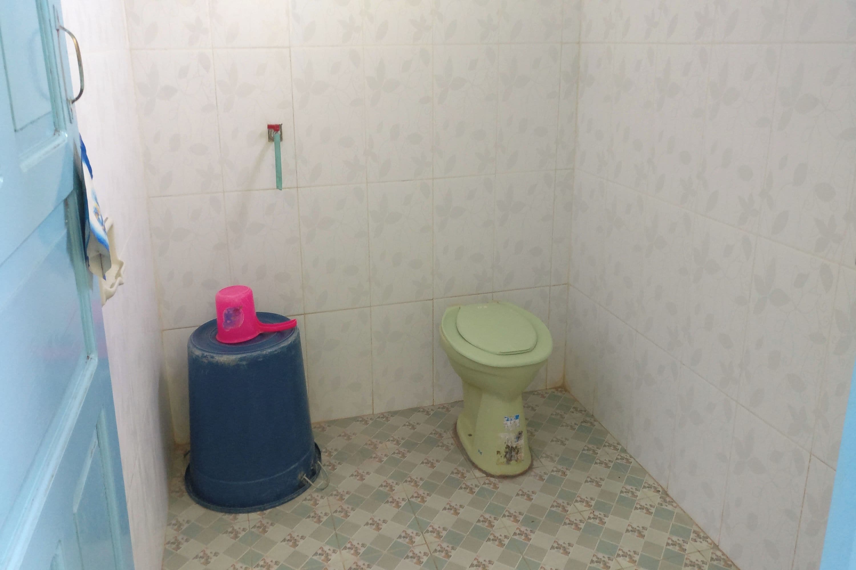 A small bathroom with a toilet, a blue barrel, and patterned floor tiles.